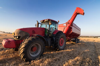 Agriculture tractor and tow trailer on a stubble field against clear sky
