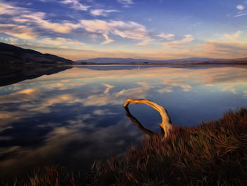 Scenic view of lake against cloudy sky during sunset