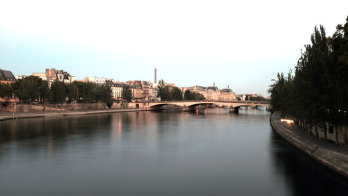 Bridge over river by buildings against clear sky