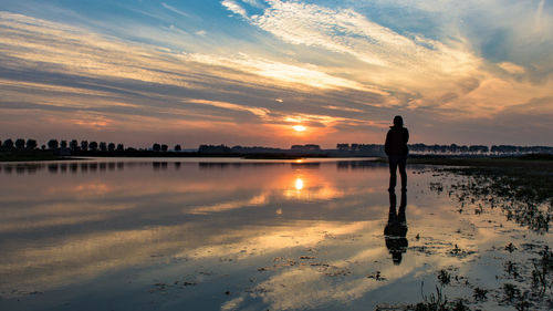 Silhouette person standing on sea shore against cloudy sky during sunset