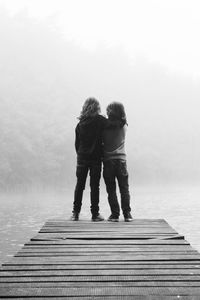 Rear view of siblings on pier over lake during foggy weather
