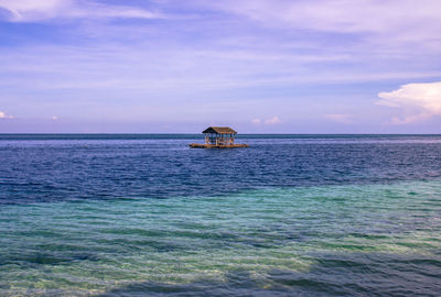 House floating on sea against cloudy sky