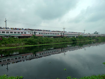 Crowd on passenger train against cloudy sky