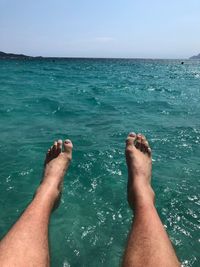 Low section of person feet in sea against sky
