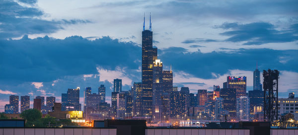 Illuminated buildings in city against cloudy sky