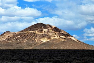 Low angle view of volcanic mountain against cloudy sky