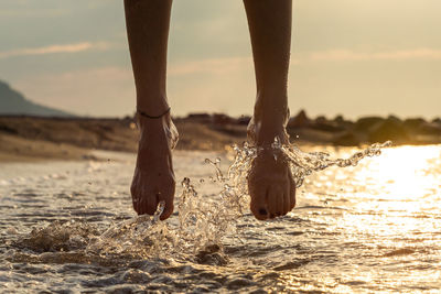Girl jumping on water sea at a beach at sunset.