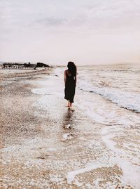 Rear view of woman standing on beach against sky