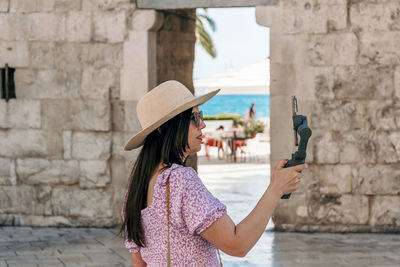 Side view of young woman using gimbal and mobile phone for vlogging on her travels.