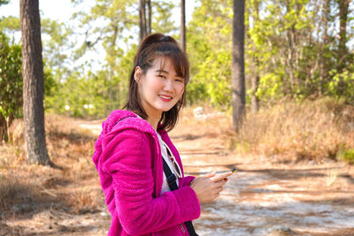 Portrait of smiling young woman using phone while standing on tree