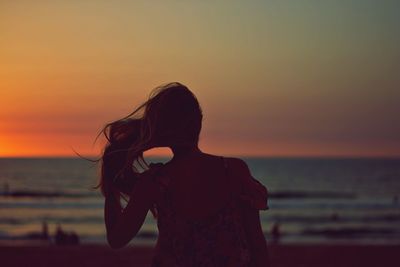 Rear view of woman standing at beach against sky during sunset