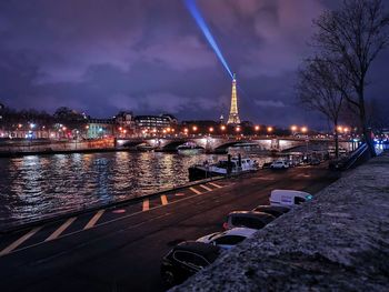 Illuminated city by river against sky at dusk