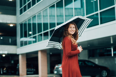 Portrait of smiling girl standing with umbrella in parking lot