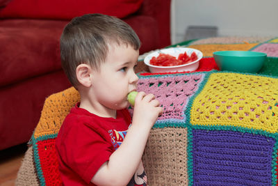 Cute toddler eating cucumbers and tomatoes while watching tv