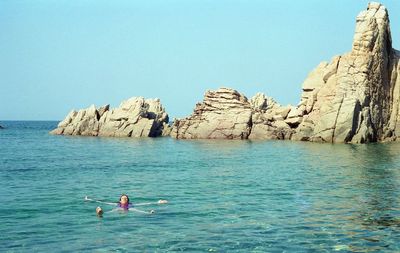 Woman swimming in sea by rock formation against clear sky