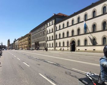 Road by buildings against clear blue sky