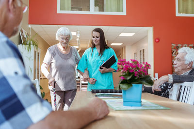 Senior woman and nurse walking arm in arm towards friends at nursing home