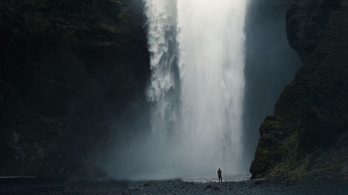 Mid distance view of person standing against waterfall