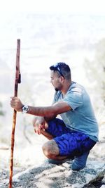 Man holding bamboo while crouching outdoors