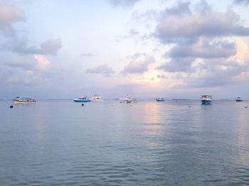 Boats sailing in sea against cloudy sky