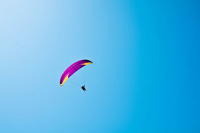 Low angle view of person paragliding against blue sky