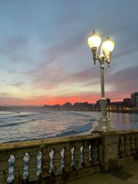 Street light by sea against sky during sunset