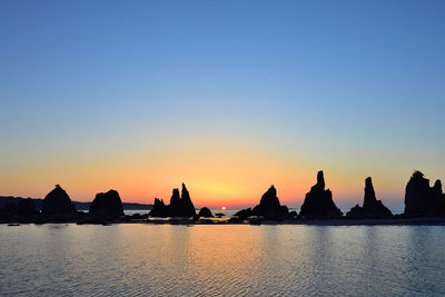 Silhouette buildings by sea against clear sky during sunset