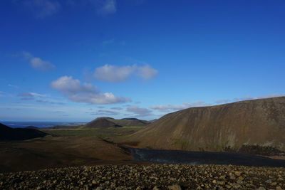 Scenic view of road by mountains against blue sky