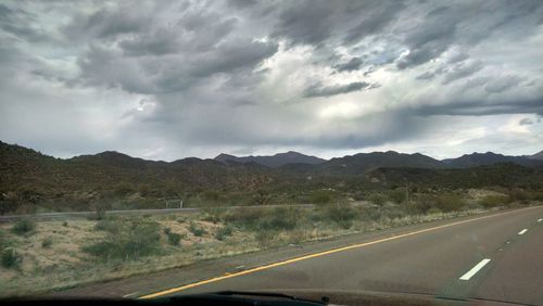 Scenic view of road by mountains against dramatic sky