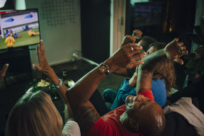 High angle view of friends cheering while watching sports on tv in living room