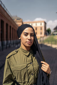 Portrait of young woman standing against building