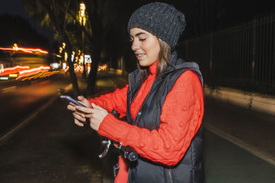 Young woman wearing warm clothing using smart phone at night