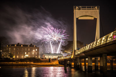 Firework display over river and bridge against sky at night