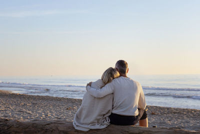 Man with arm around woman looking at sunset on beach