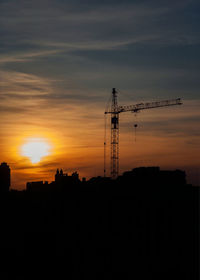 Silhouette crane at construction site against sky during sunset