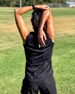 Rear view of woman exercising while standing on field