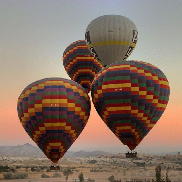 hot air balloon, flying, mid-air, clear sky, transportation, parachute, sky, copy space, travel, multi colored, outdoors, ferris wheel, low angle view, air vehicle, adventure, landscape, tourism, built structure, no people, travel destinations