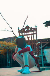 Low angle view of man with pot covered face crouching against sky