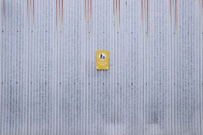 Yellow sign on corrugated metal wall.