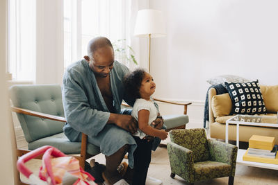 Father holding crying daughter while sitting in living room at home