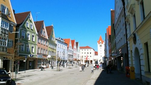 People on street amidst buildings in city against clear blue sky