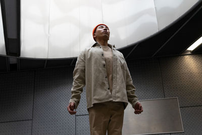 Low angle view of young man looking away against wall