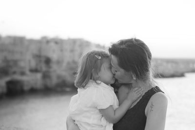 Close-up of mother kissing by daughter by river against sky