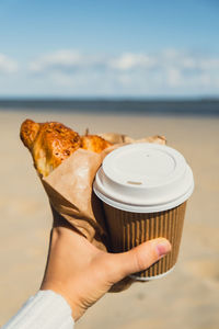 Cropped hand of woman holding coffee at beach