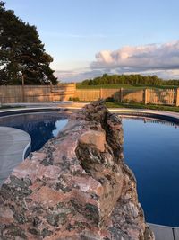 Rocks by swimming pool against sky during sunset