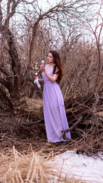 Young woman standing against bare tree