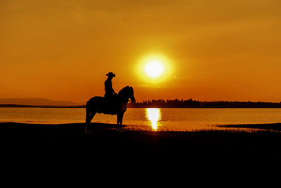 Silhouette man riding horse at sunset