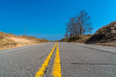 Surface level of road against clear blue sky