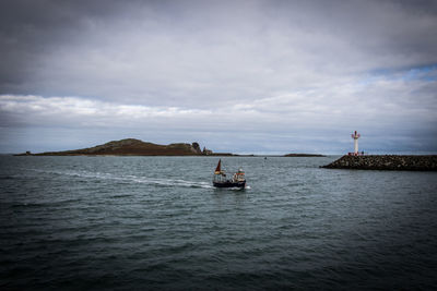 Boat sailing in sea against cloudy sky