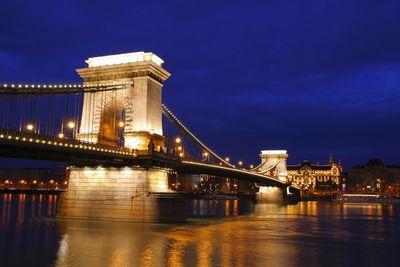 Illuminated bridge over river against sky in city at night